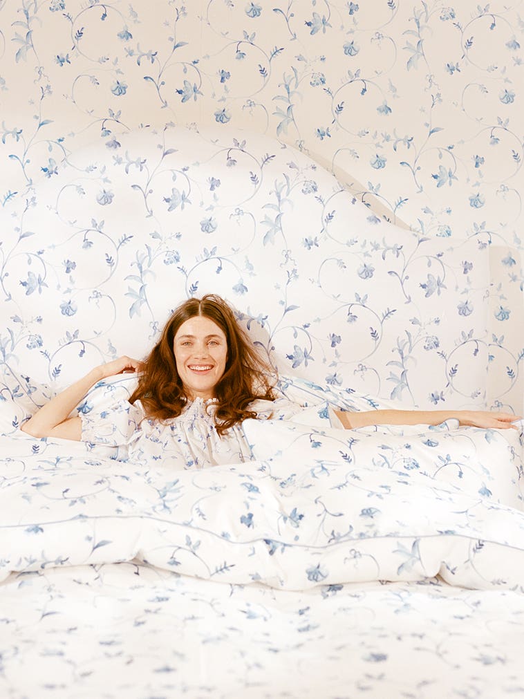 Woman lying in bed; White duvet cover, pillows and wallpaper with liberty blue flowers