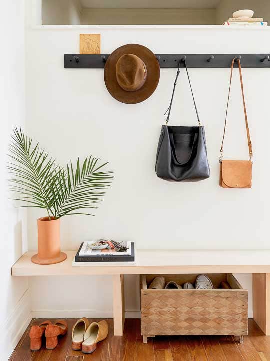 entryway with bags and a hat hanging, a white bench and a basket underneath the bench