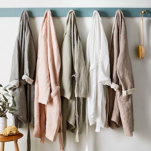 Four cotton bathrobes hanging up on wall hooks in bathroom