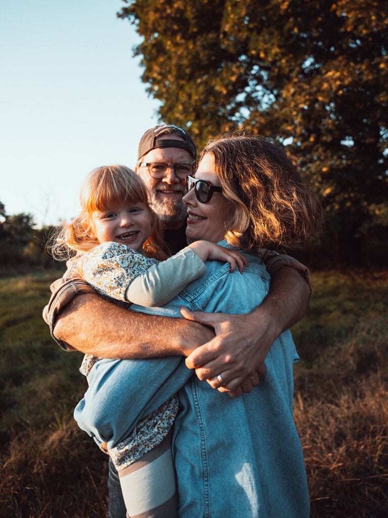 mom, dad, and daughter hugging outdoors