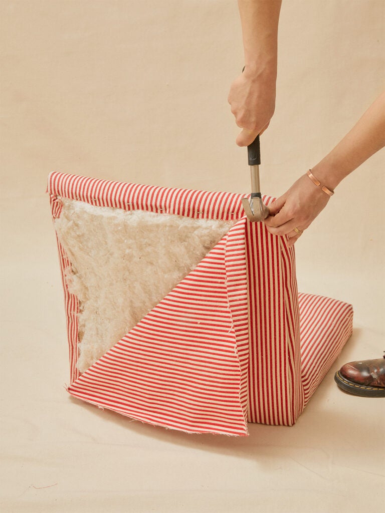 hand hammering nail into red and white striped fabric on chair back