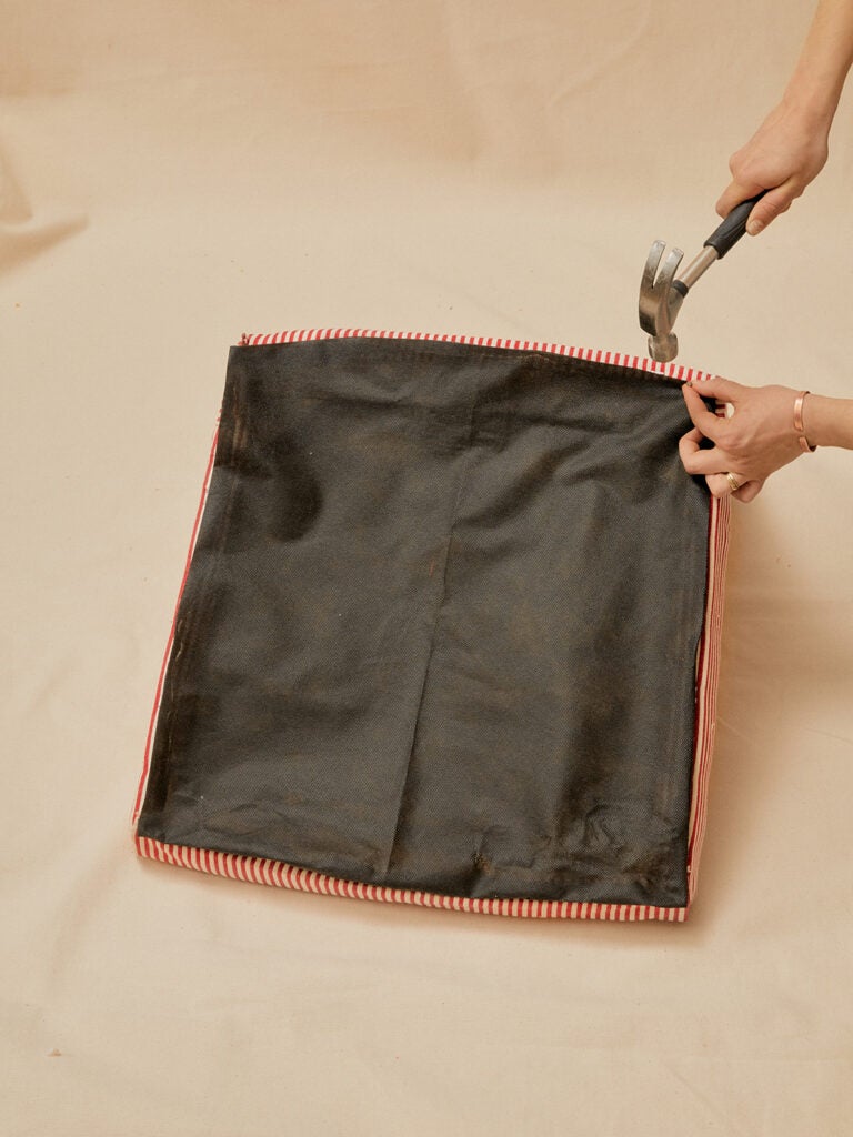 hammering nail in black fabric on bottom of reupholstered chair