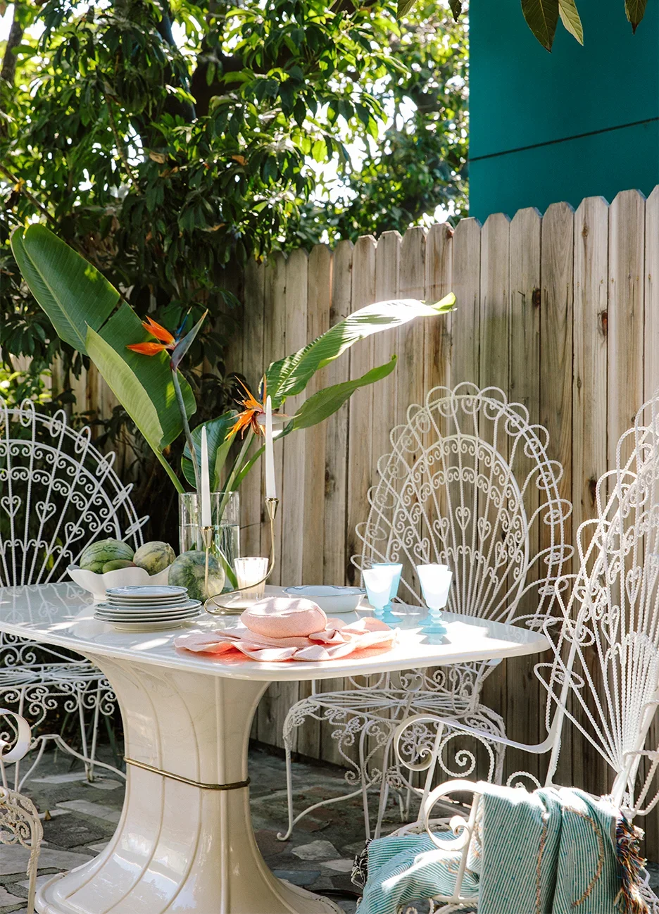 White patio furniture and vintage table in fenced backyard with clippings of Bird of Paradise