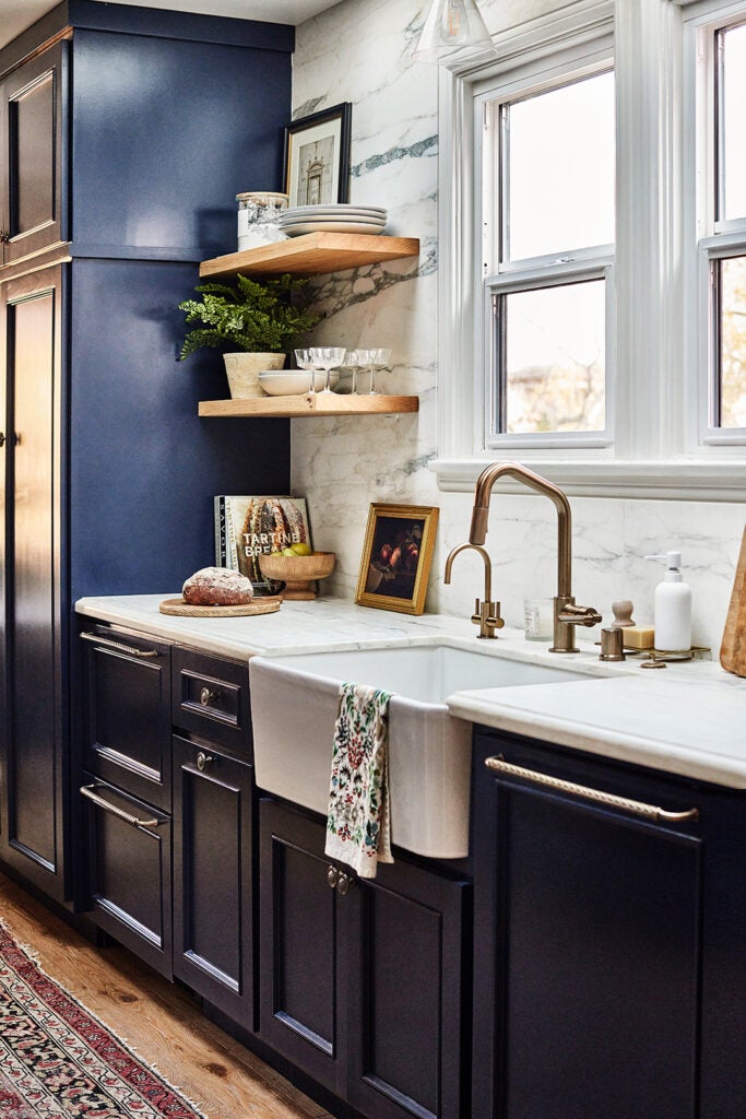 Kitchen sink surrounded by dark blue cabinets and white windows.