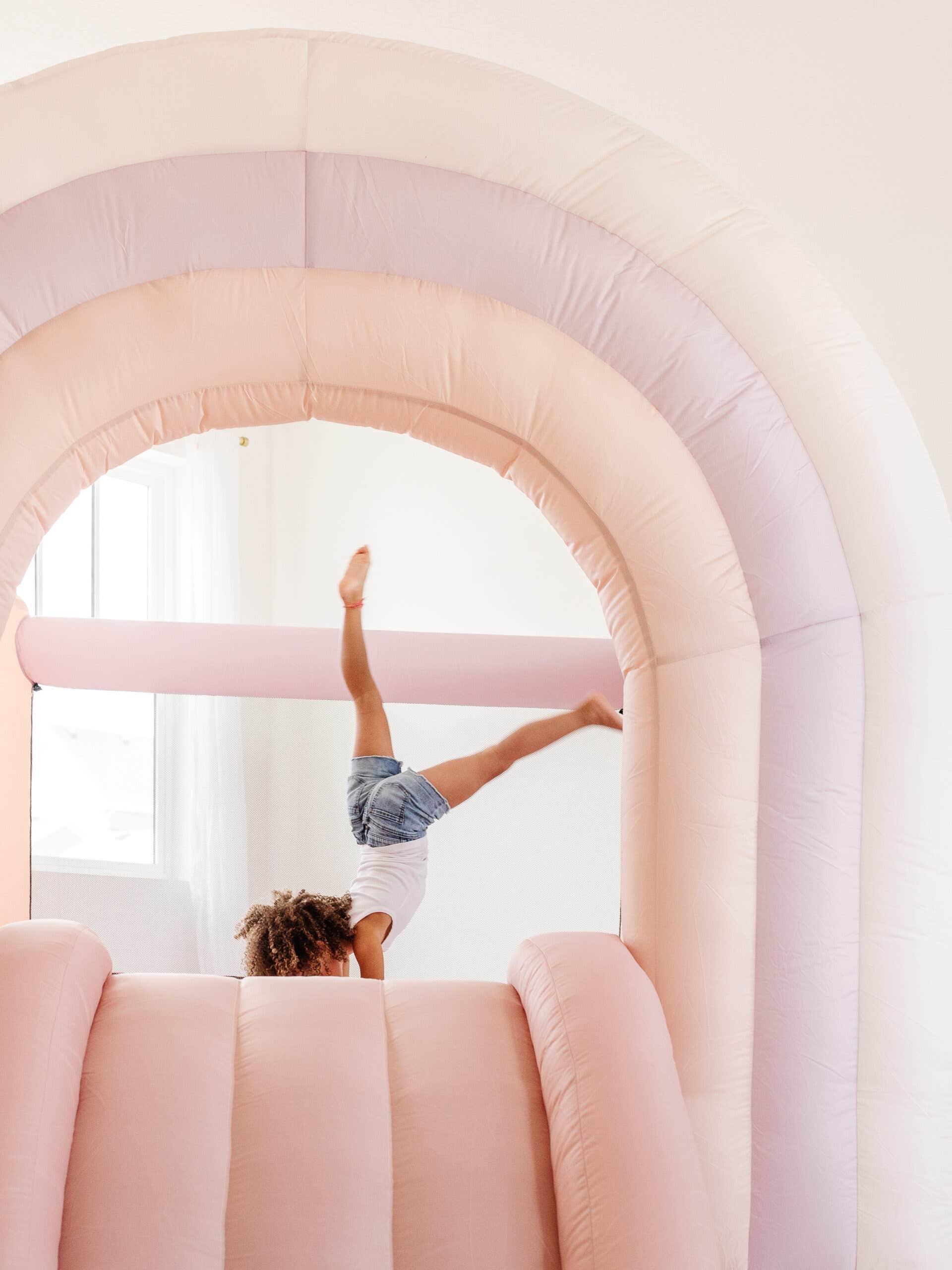 child on pale pink rainbow-shaped bounce house