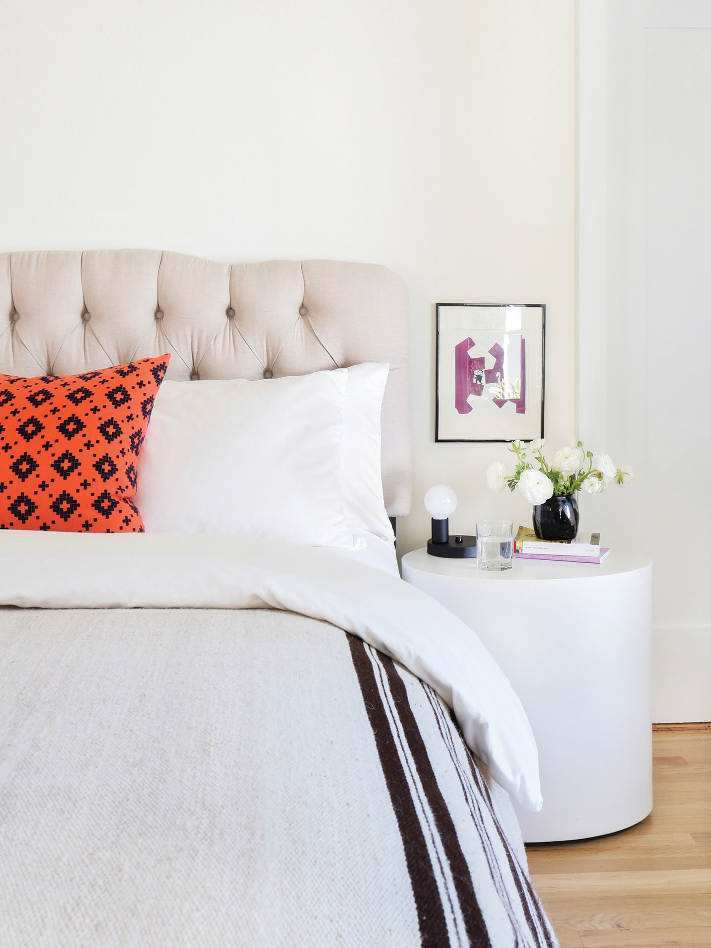 Bed ith Orange Pillow and Round Side Table and Tufted Headboard