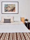 bed with light gray duvet cover three rows of pillows and patterned throw blanket