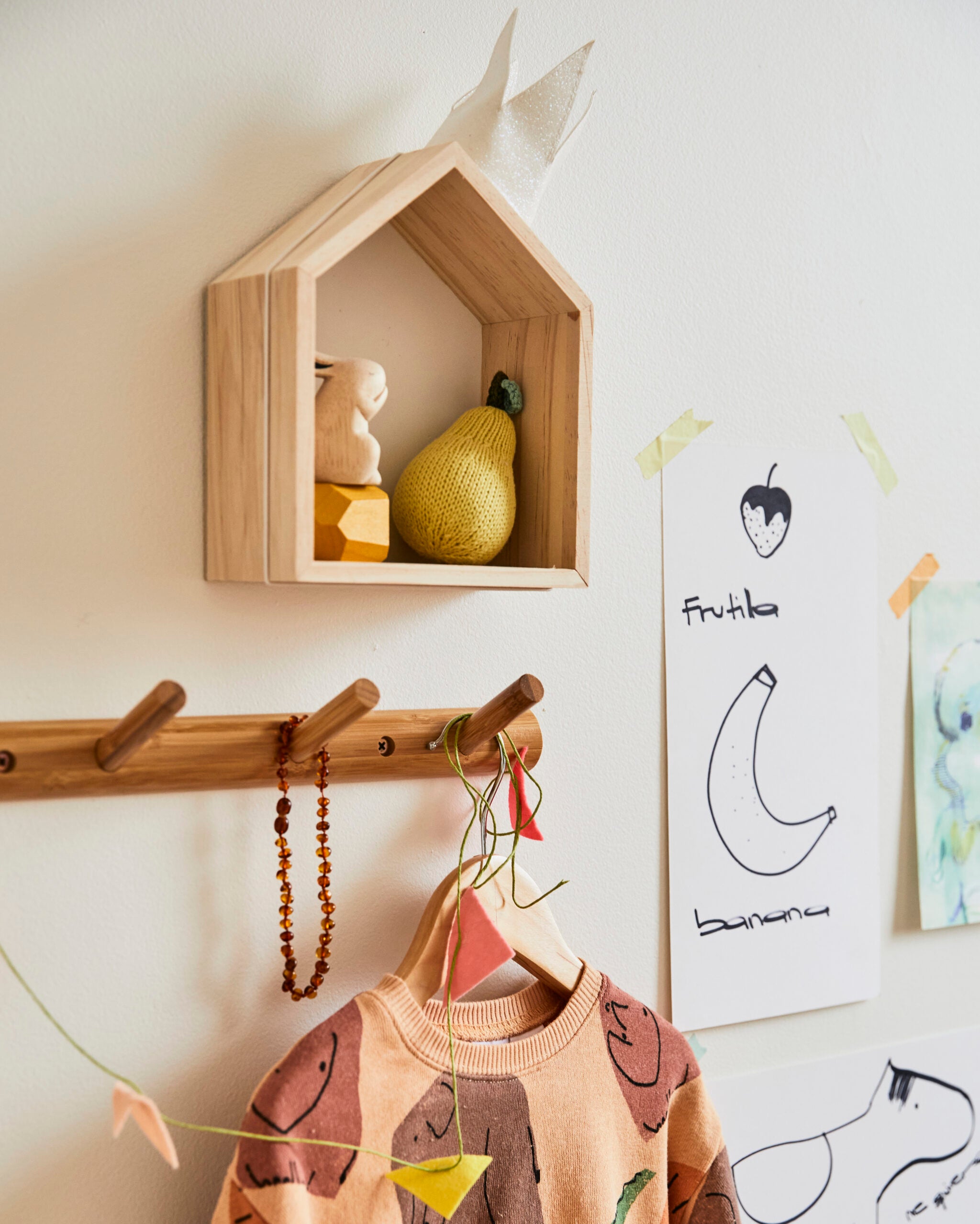 Wood house-shaped shelf above wood peg rail in kid’s room