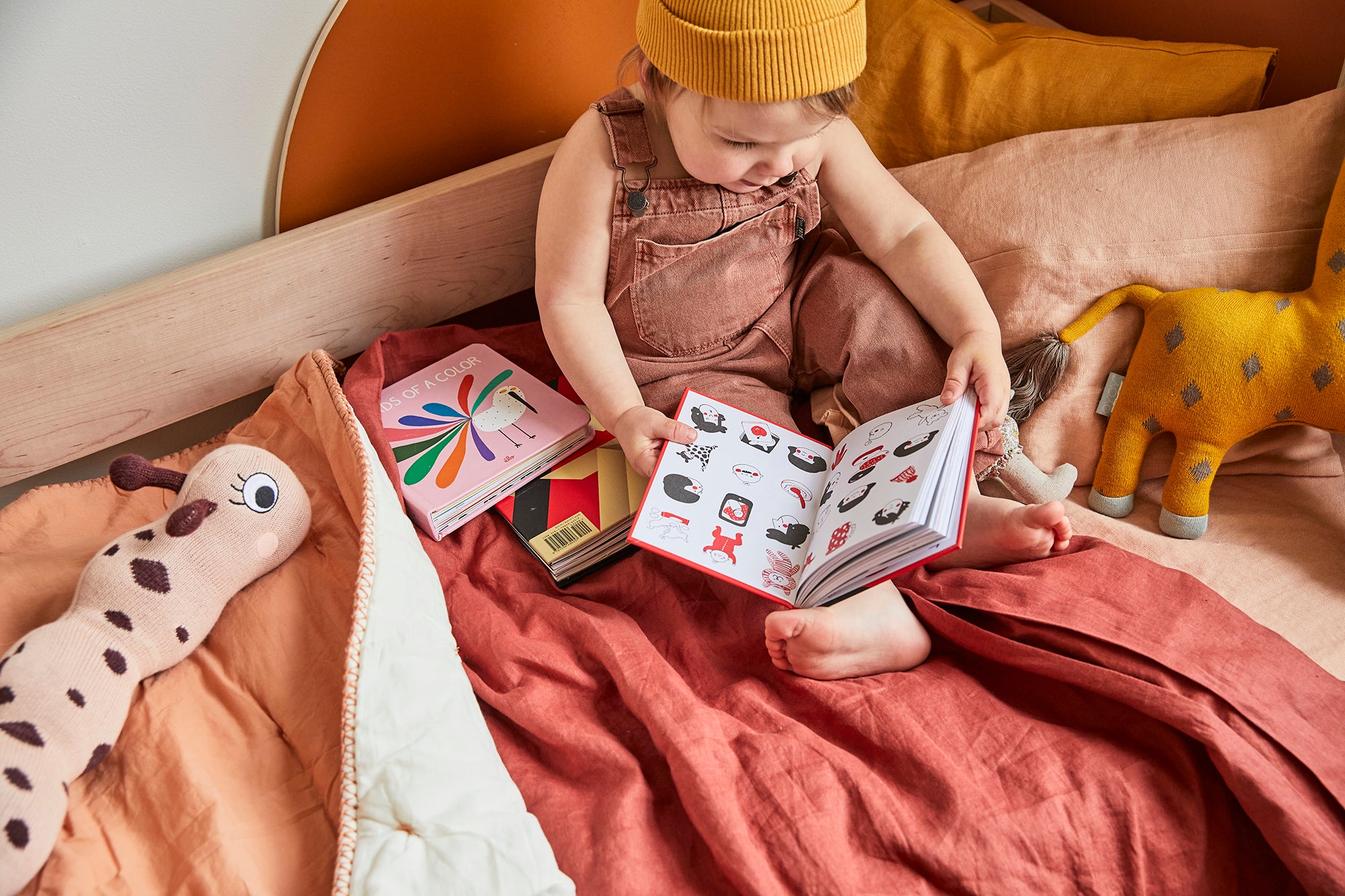 toddler on wood bed with sunset-colored bedding reading a book
