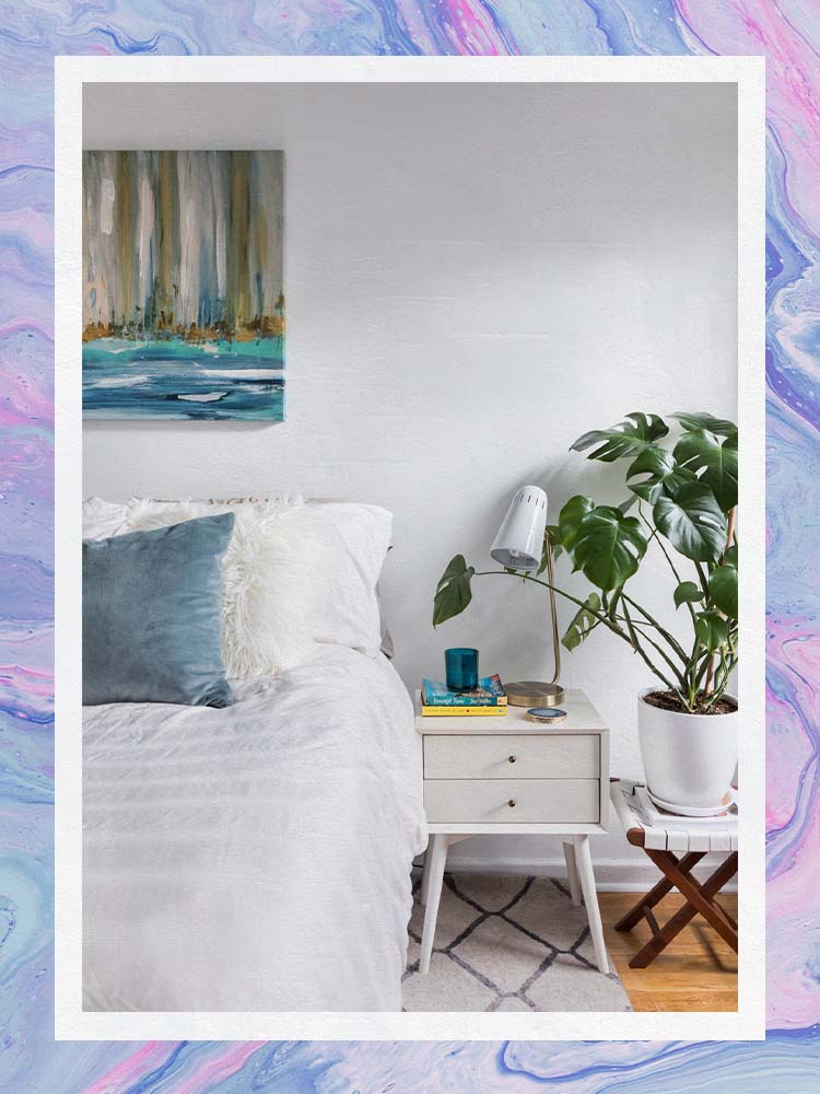 white bedroom with mattress and blue pillow with monsterra plant and plnater