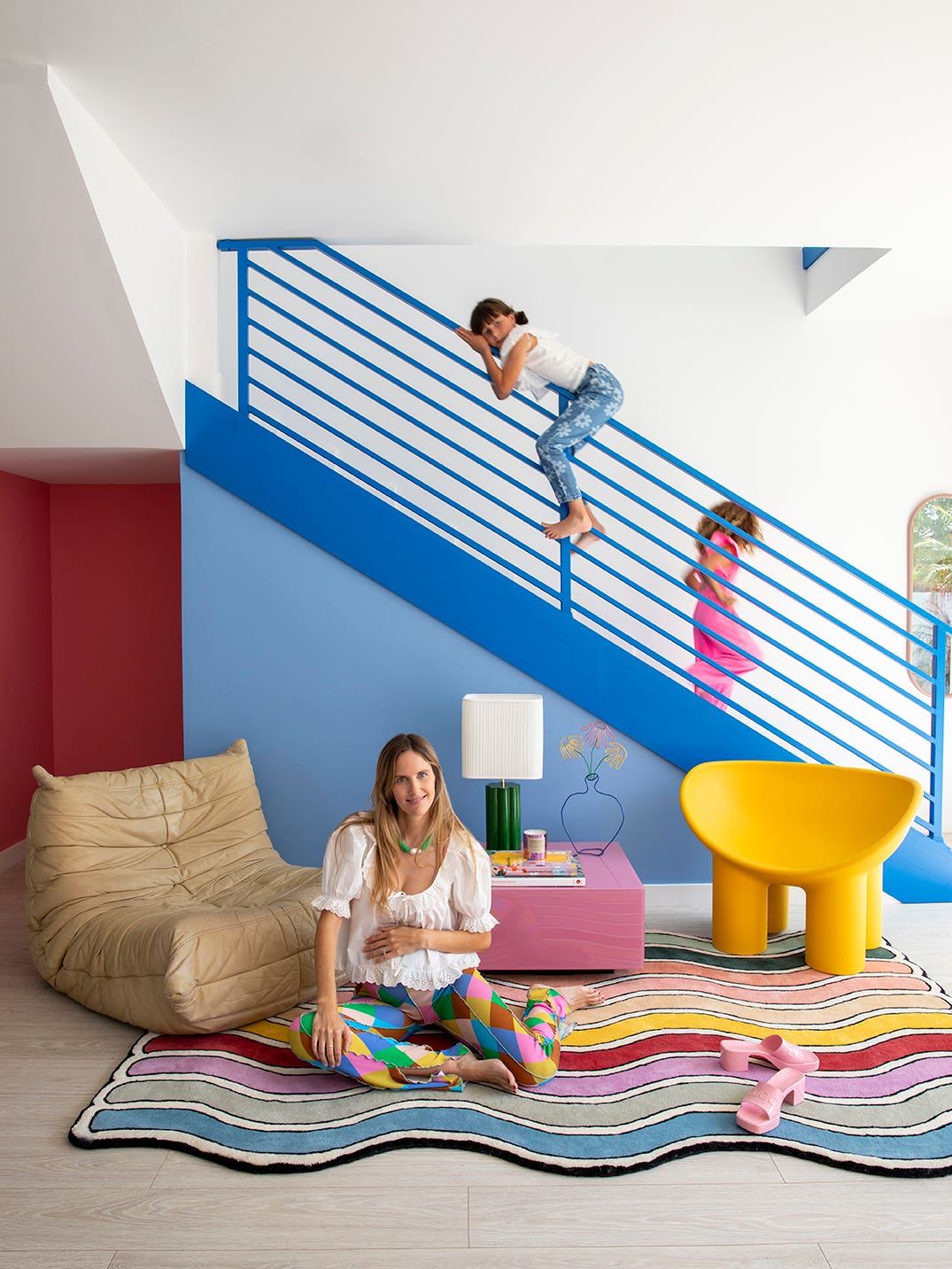 kids playing on blue metal staircase; mom sitting on rainbow rug