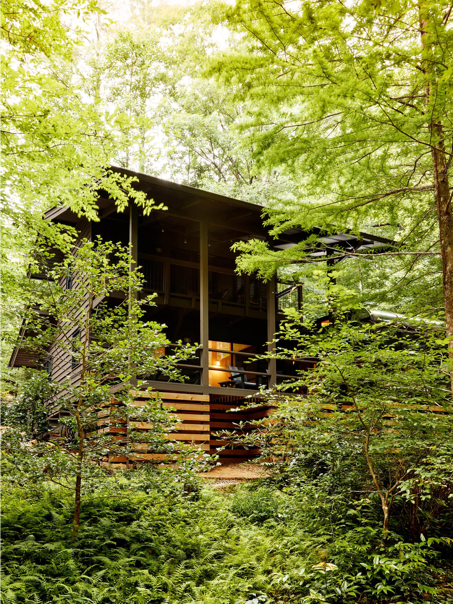Black painted home and wooden front porch surrounded by green, leafy trees in the woods