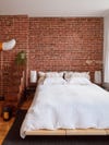 Bed with white sheets against brick wall