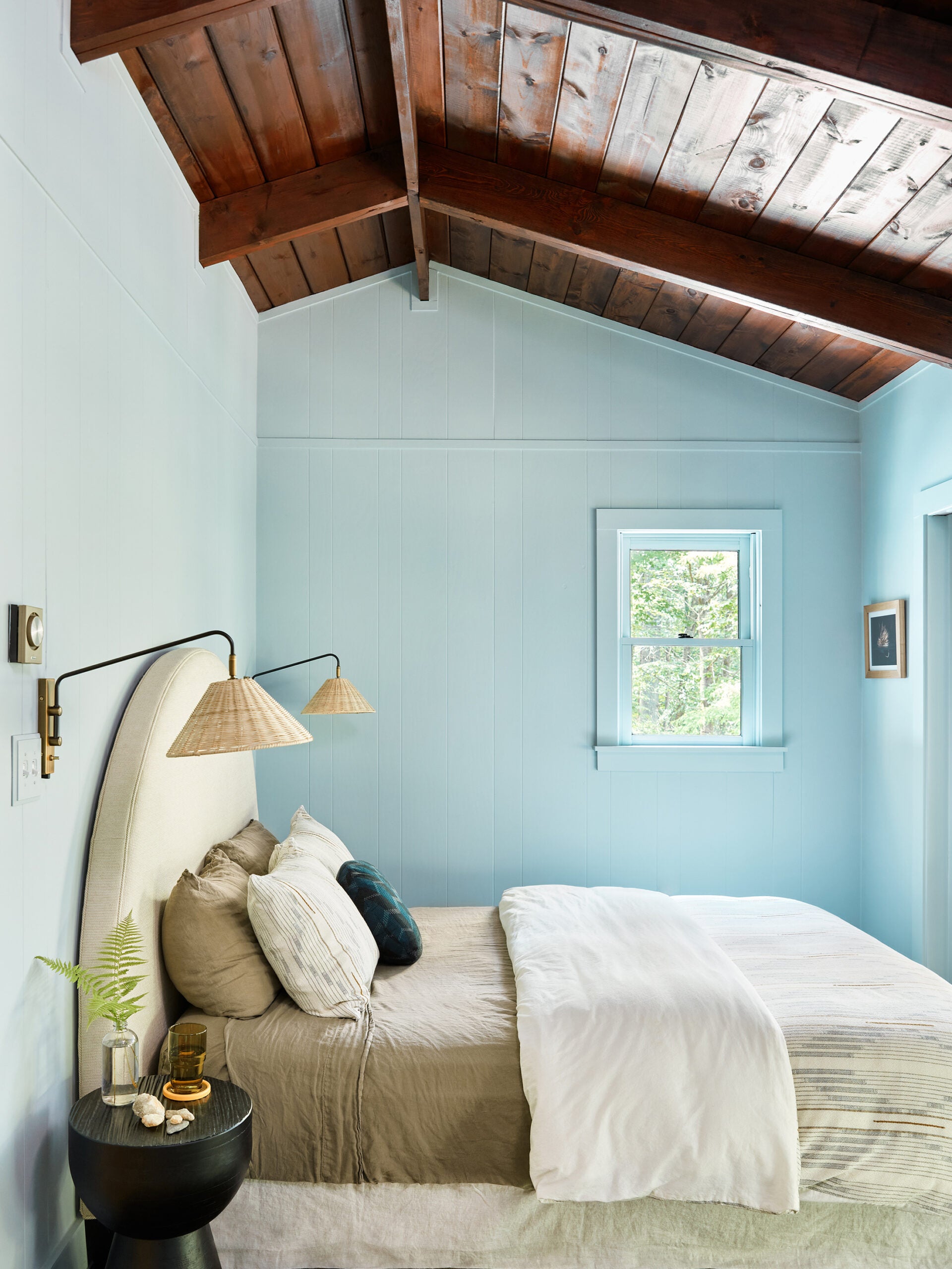 Blue painted wood panel walls and wood ceiling with round bed frame flanked by rattan wall sconces