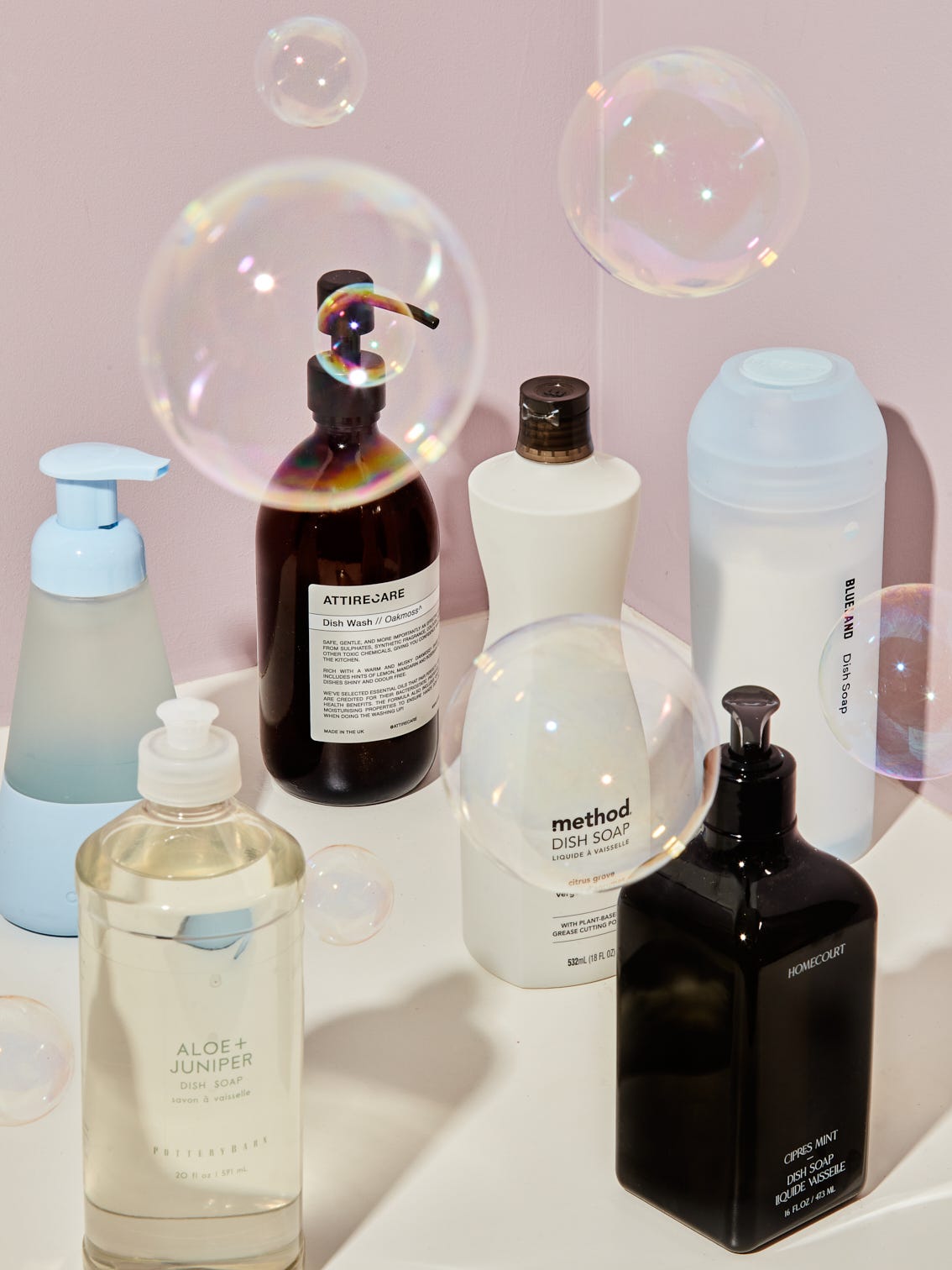 bunch of dish soaps surrounded by bubbles in front of pink background