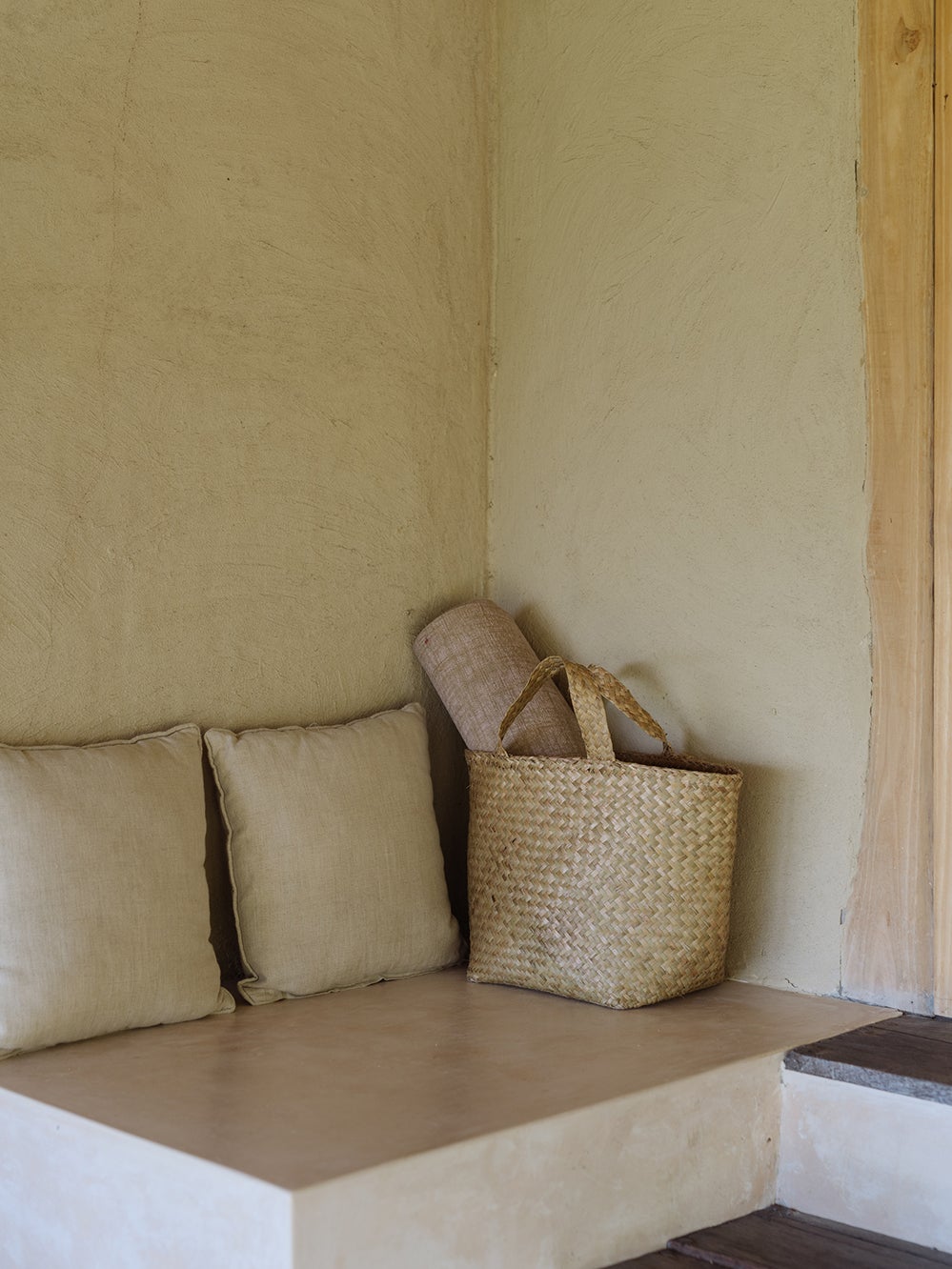 Natural woven bag with yoga mat inside stands against the wall next to the pillow