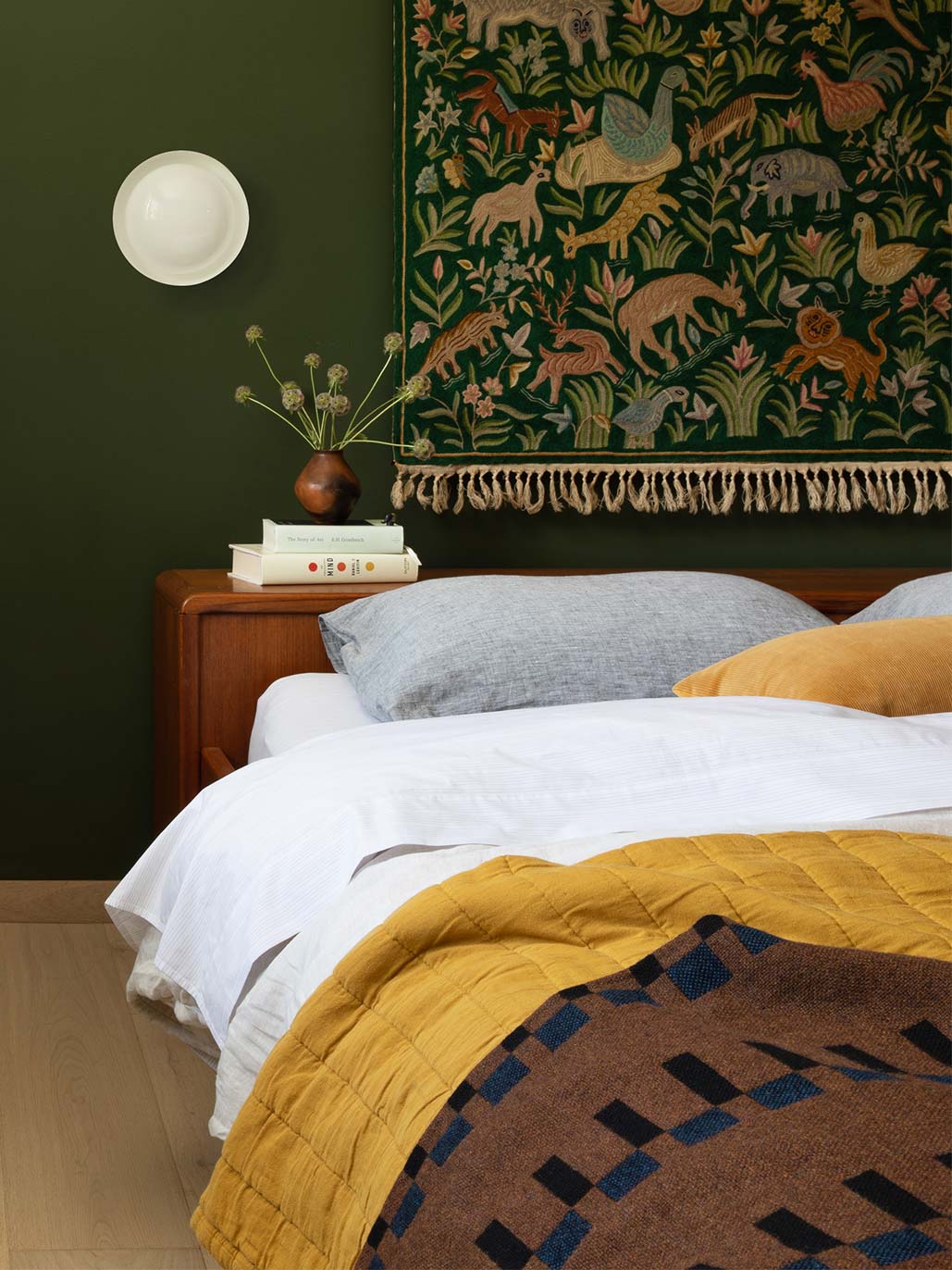 green bedroom with yellow quilt and tapestry hung as a headboard