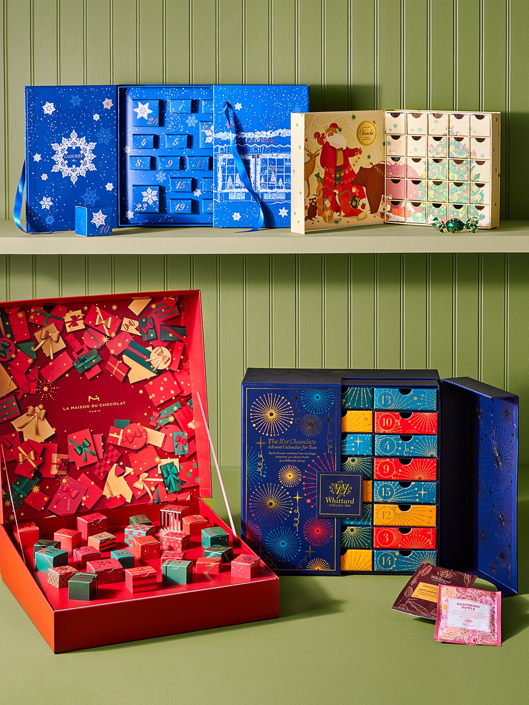 Multiple Advent Calendars in Blue, Red, and Mulit-colored Boxes from Food52 Opened in front of Green Slatted Wall