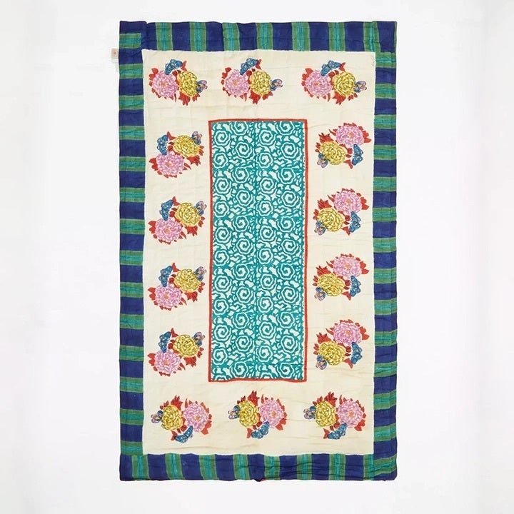 Quilt with block-printed florals and blue stripes flat against a white background.