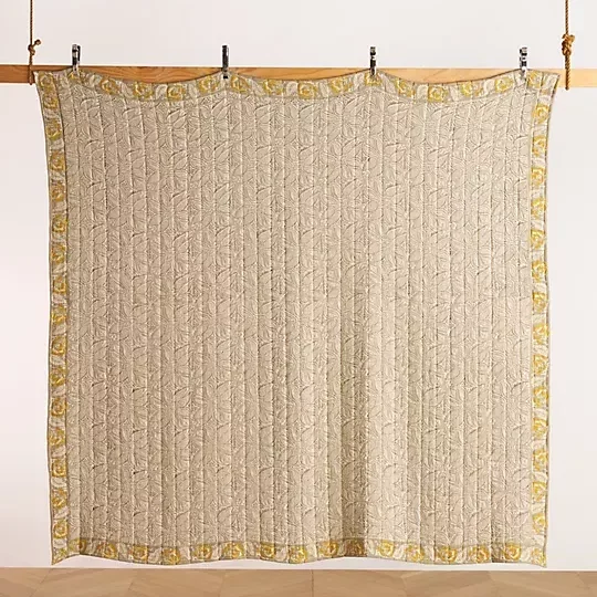 Neutral beige paisley patterned quilt hung by clothespins on a wooden beam.