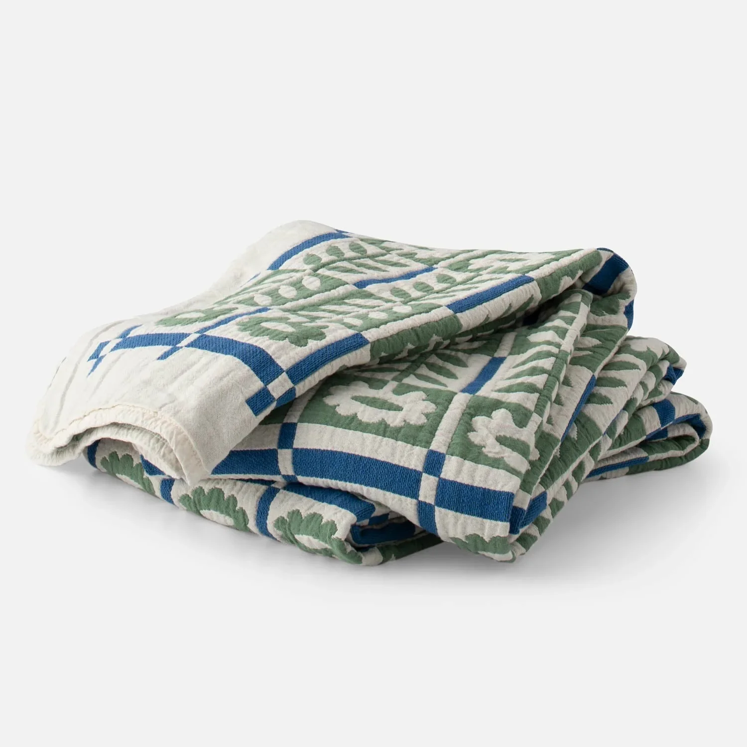 A folded olive, white, and cerulean blue floral quilt amidst a white background.