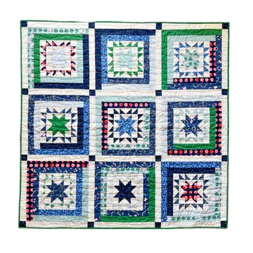 Geometric cobalt blue, evergreen, navy, and white patchwork quilt in front of a white background.