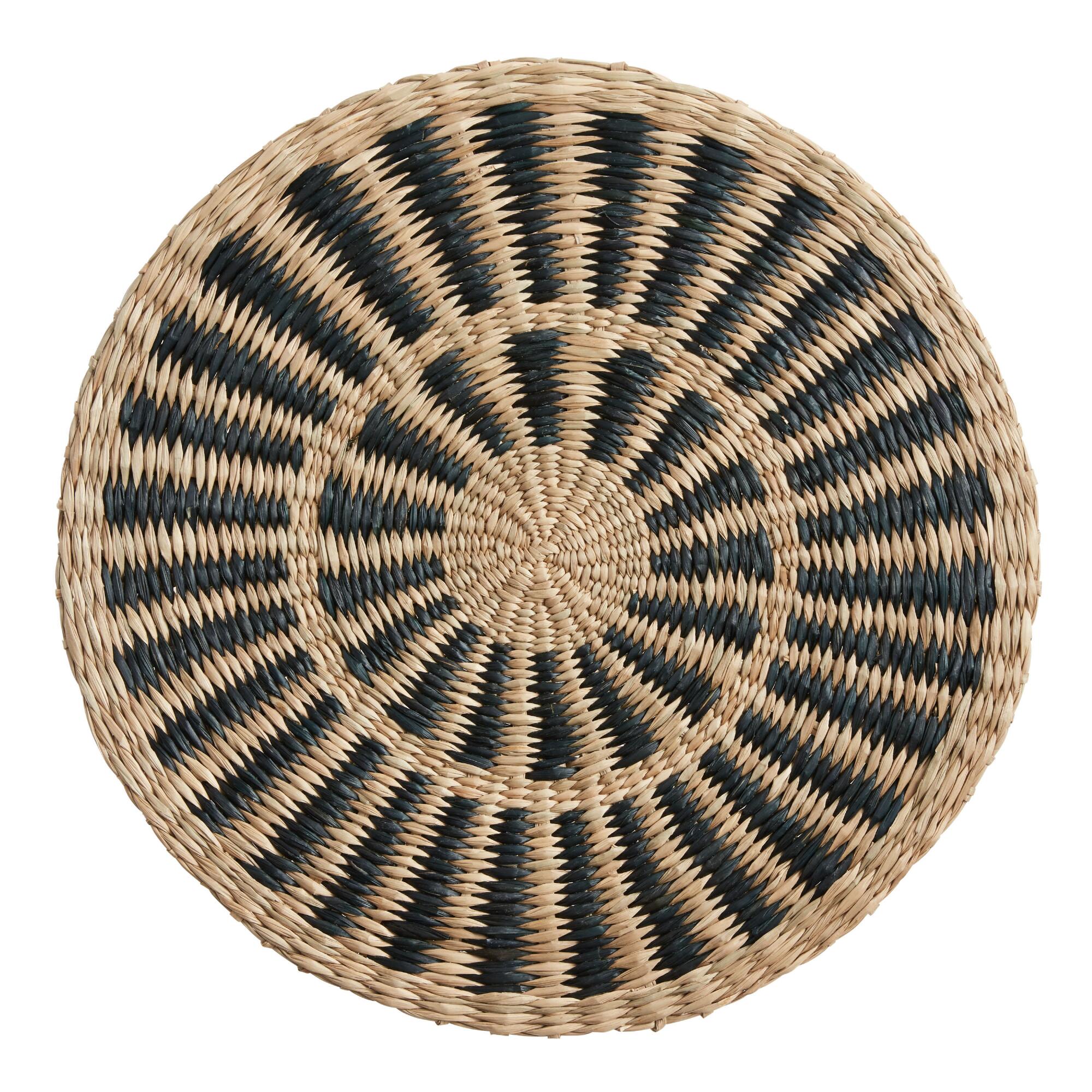 Round natural and black woven fiber placemat against a white background.