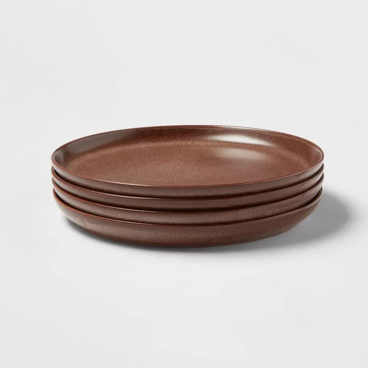 Four brown slightly distressed glazed stoneware plates stacked atop each other against a white background.