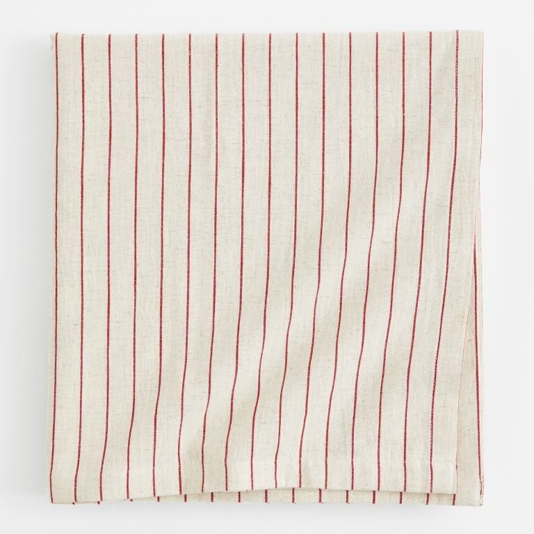 Off white linen tablecloth with thin red stripes folded into a square against a white background.