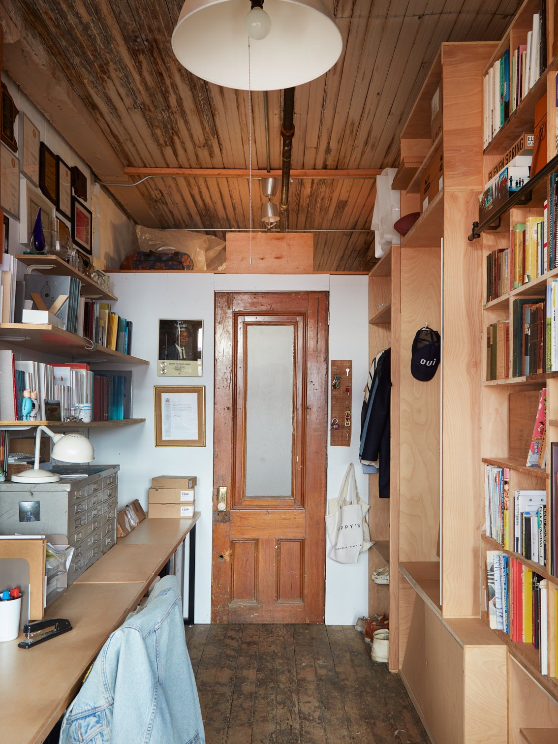 An hallway with wooden book shelves on both sides and a narrow wooden door at the end.