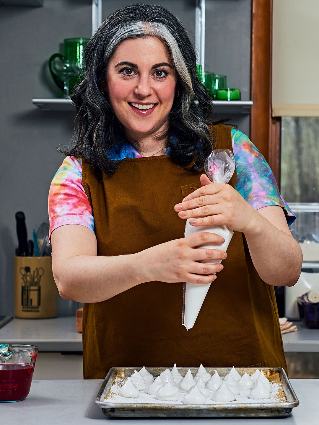 Claire Saffitz wearing a brown apron and making meringues on a kitchen island.