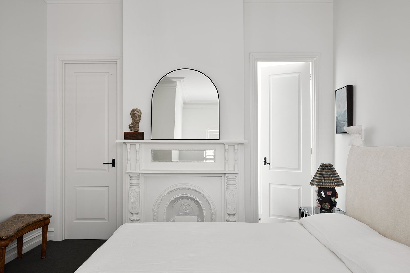 white wall bedroom with original fireplace and arched mirror on mantel