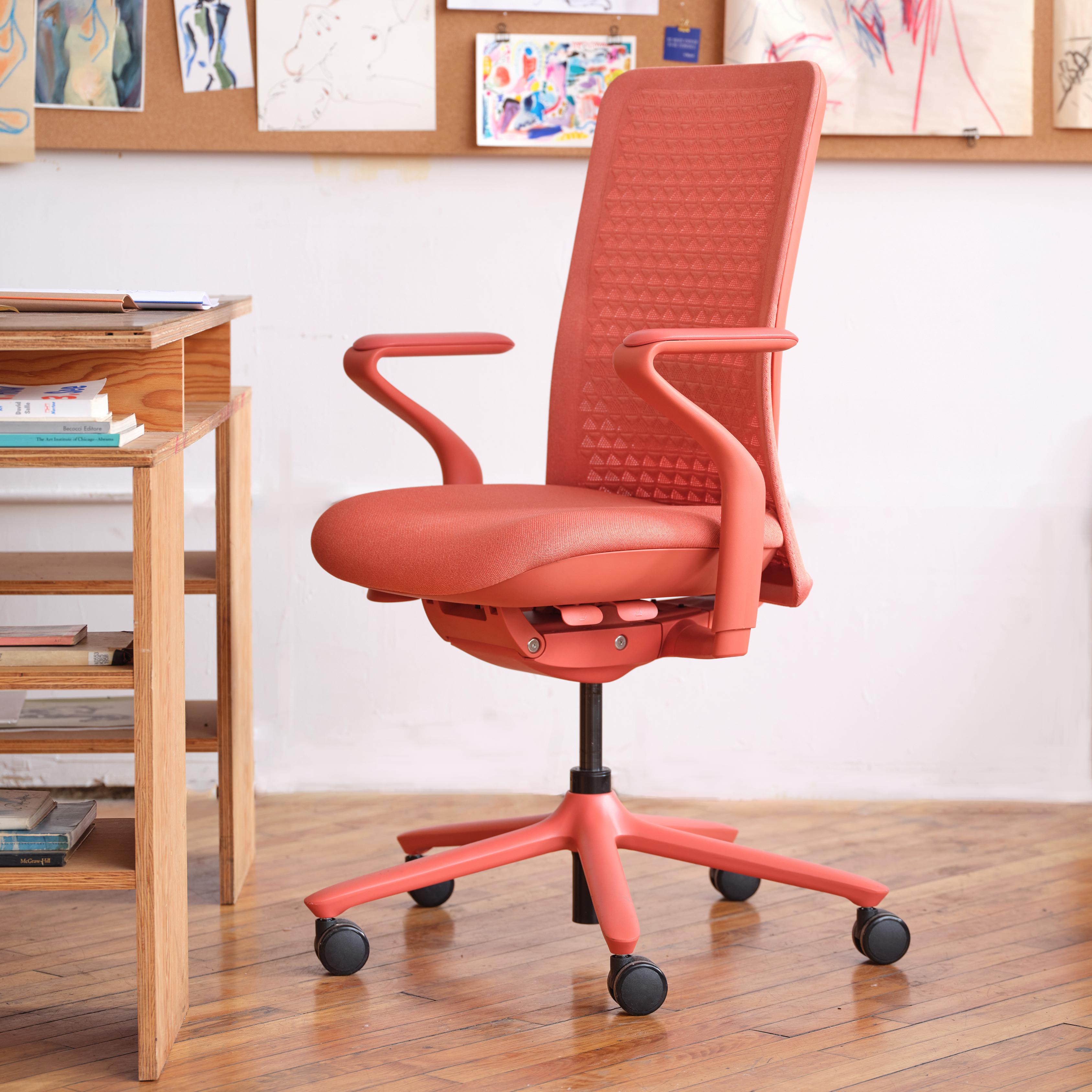 The coral-colored Verve Chair in front of a wooden desk setup.