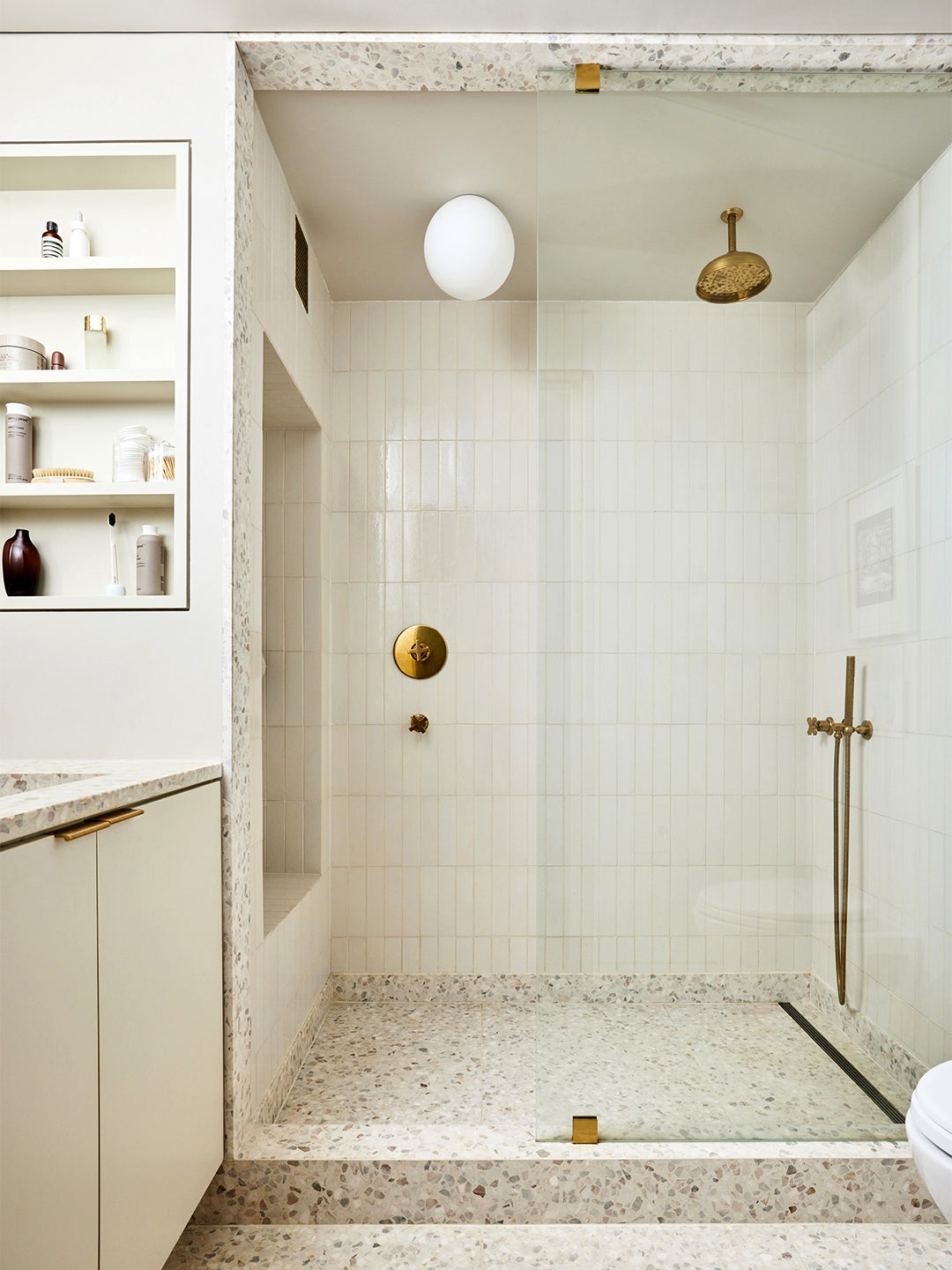 white tile and terracotta flooring in shower with brass plumbing fixtures with inset shelf