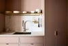 kitchen sink and surrounding cabinetry with marble backsplash and matching counters with brass shelf above