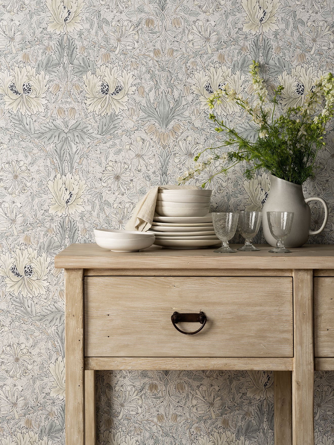Floral wallpaper behind wood console table decorated with tableware and vase of flowers