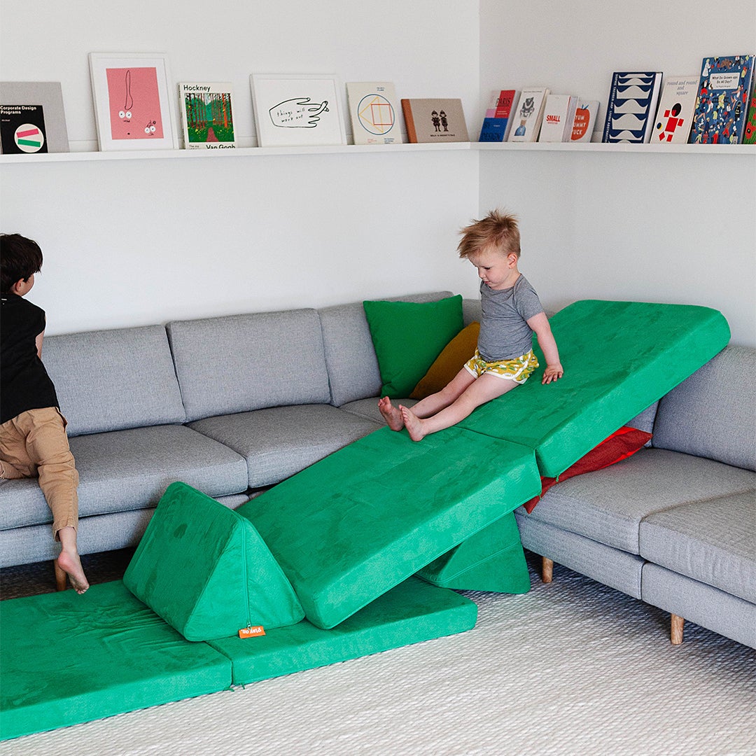 child sliding down green cushion slide