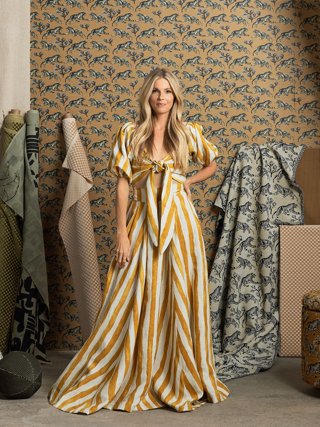 Sarah Sherman Samuel in white and yellow striped dress standing in front of fabric rolls with her new patterns for Lulu and Georgia