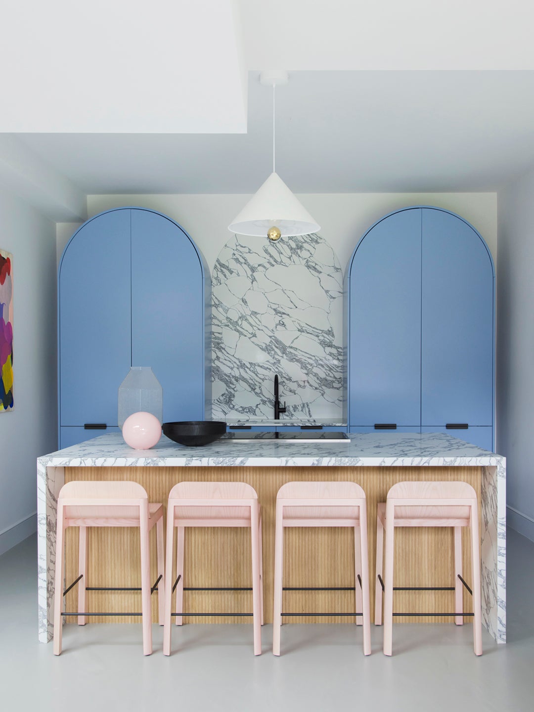 Kitchen with arched blue cabinets, marble counter, and pink stools.