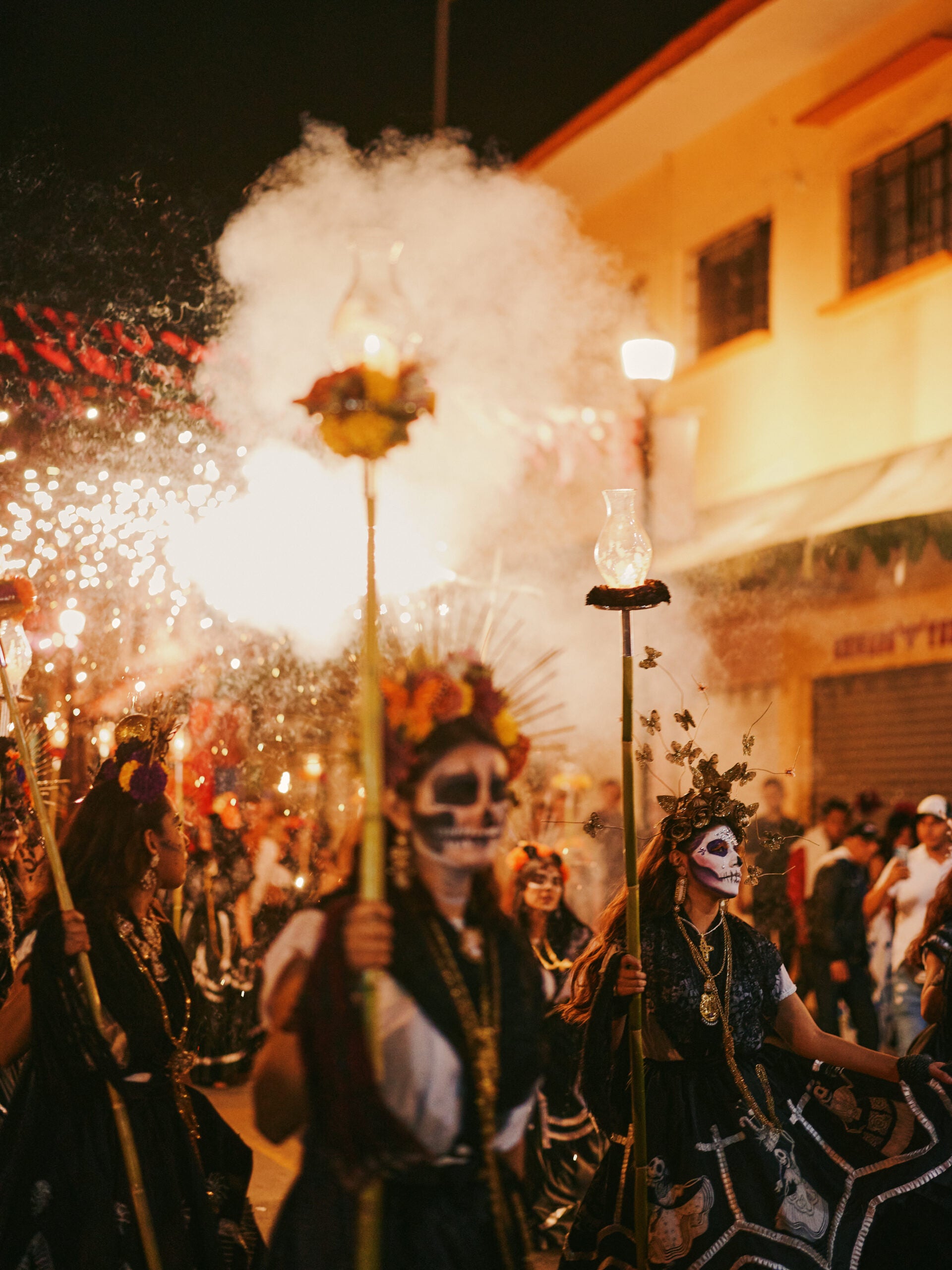 People parading down street holding sparklers and wearing face paint for Day of the Dead in Mexico.