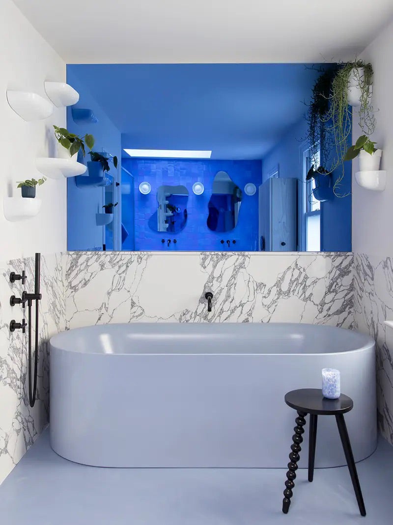 Bathroom with blue tub, floor, and reflective mirror-like surface on the wall. 