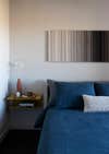 Felt art piece hanging above bed with blue linen sheets.