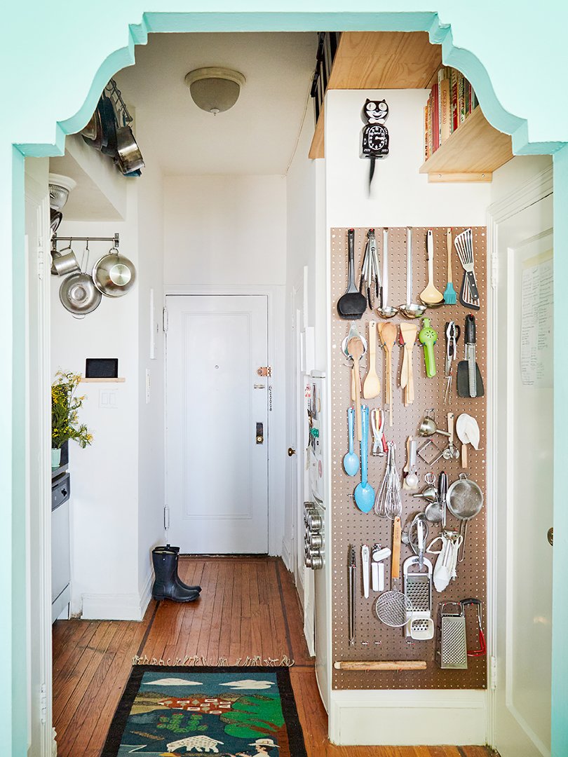 A sculptural case opening lead to a galley kitchen where cooking tools are organized on a  pegboard