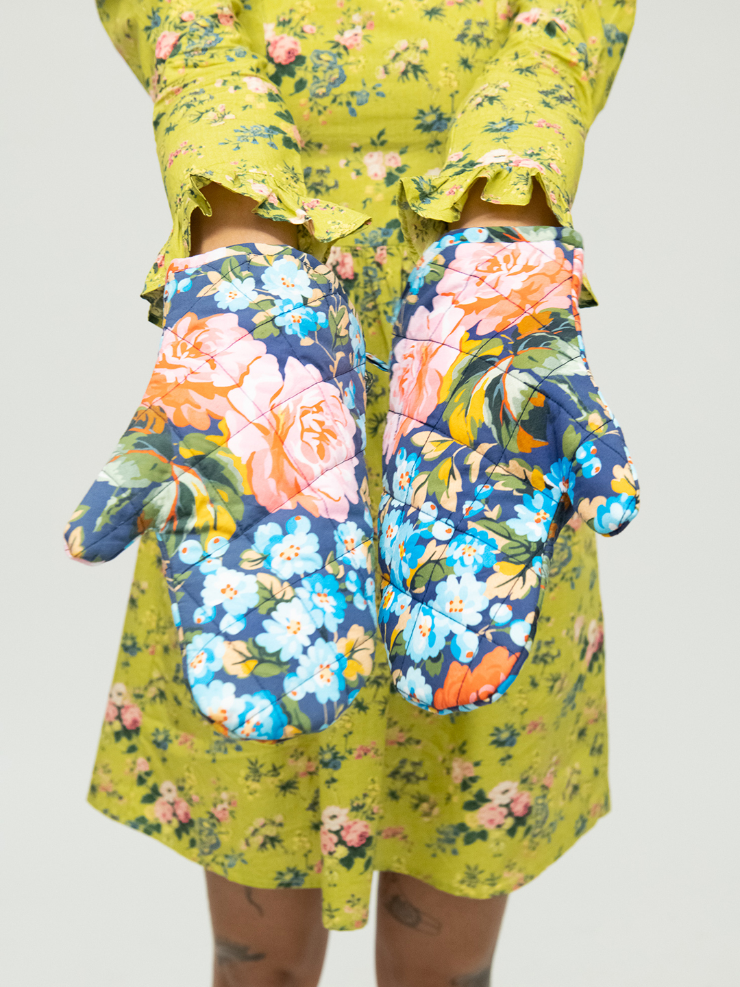 woman in floral dress with blue oven mitts.