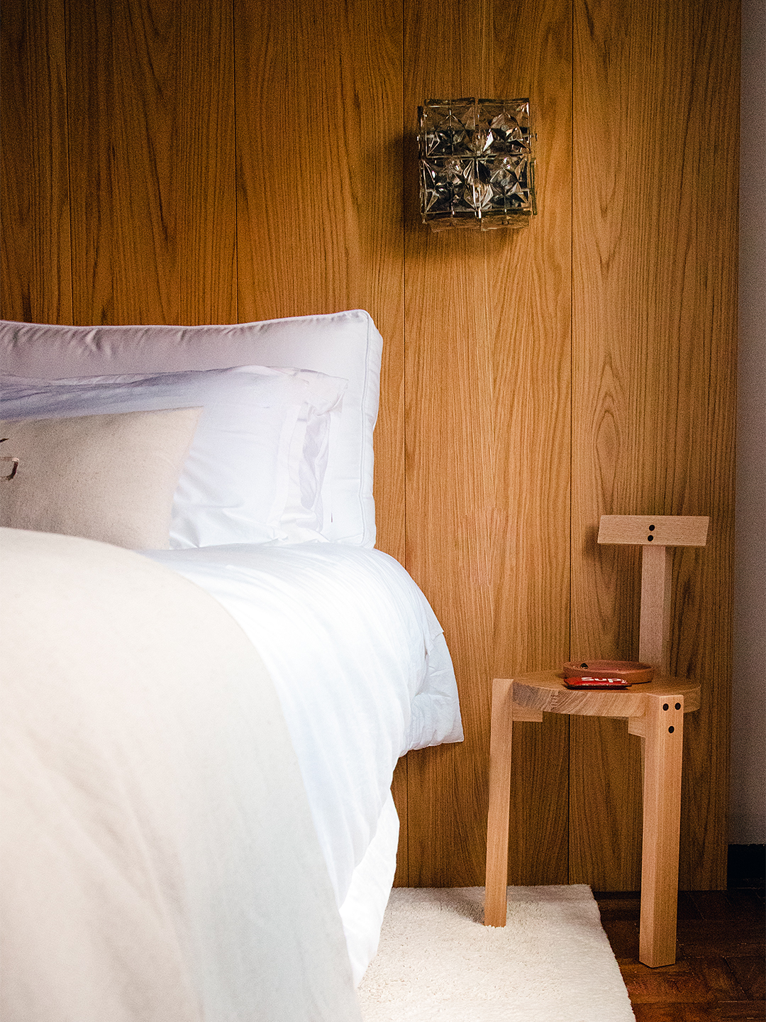 Bed with white linens against wood paneled wall
