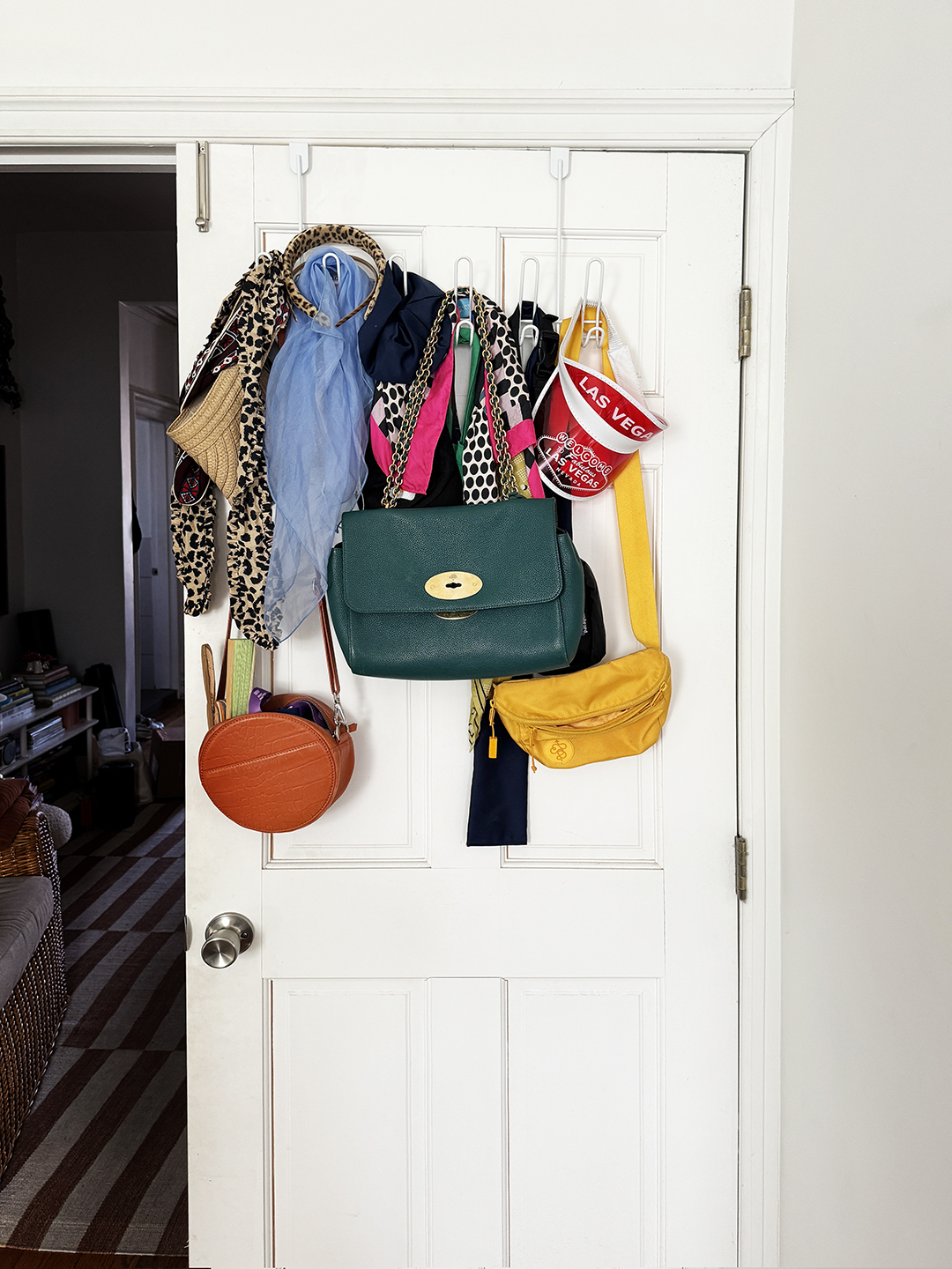 Purses, scarves and totes hanging messily on the back of a door