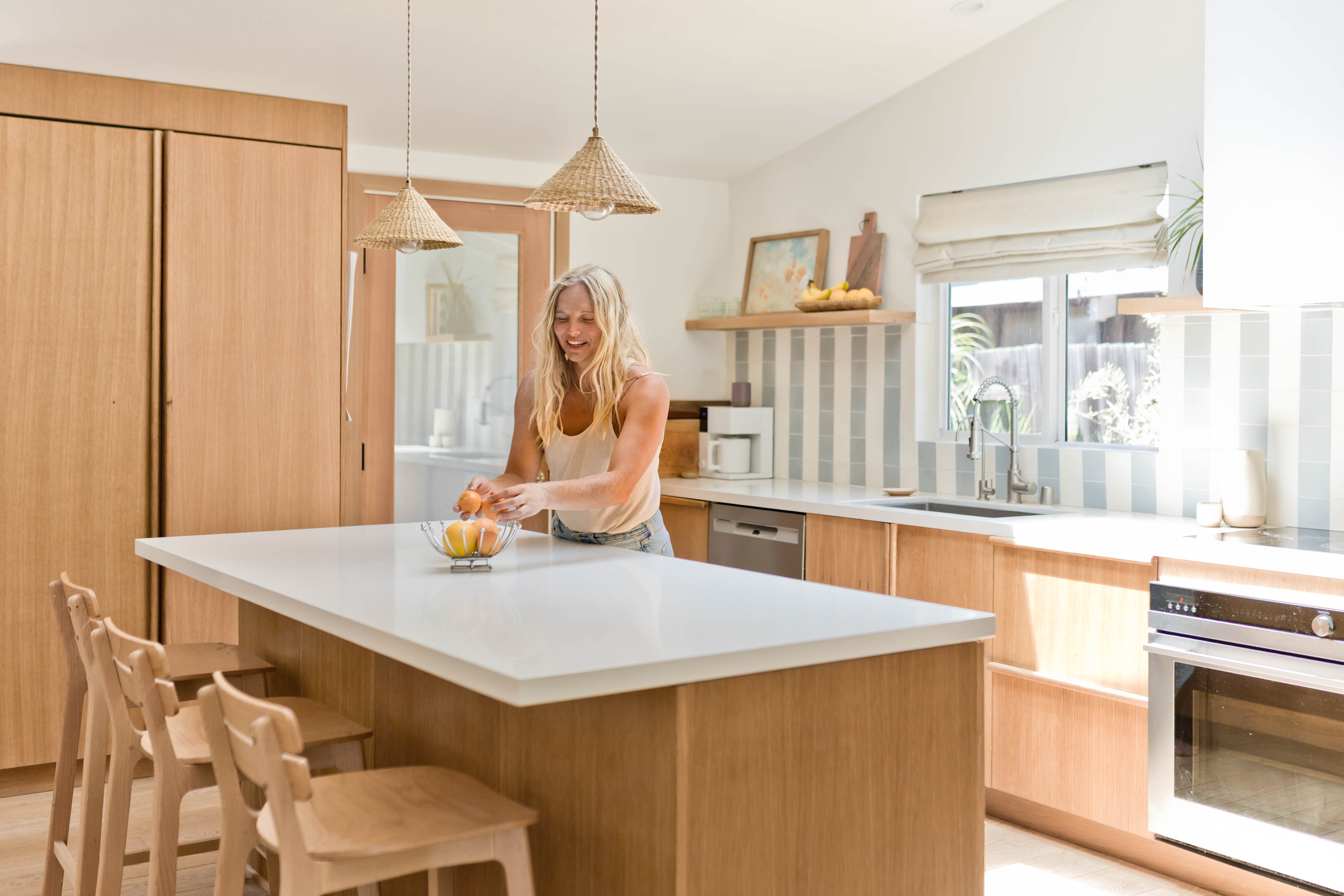 Woman at her white stone kitchen counter filled with wood and striped tile accents. 