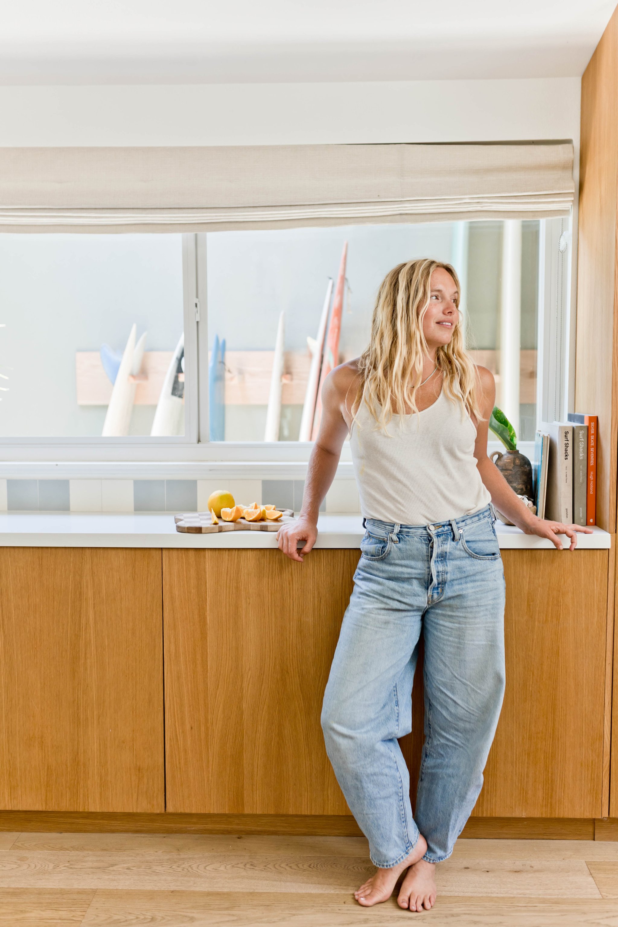 Woman wearing jeans in her kitchen with warm wood cabinetry and picture window.
