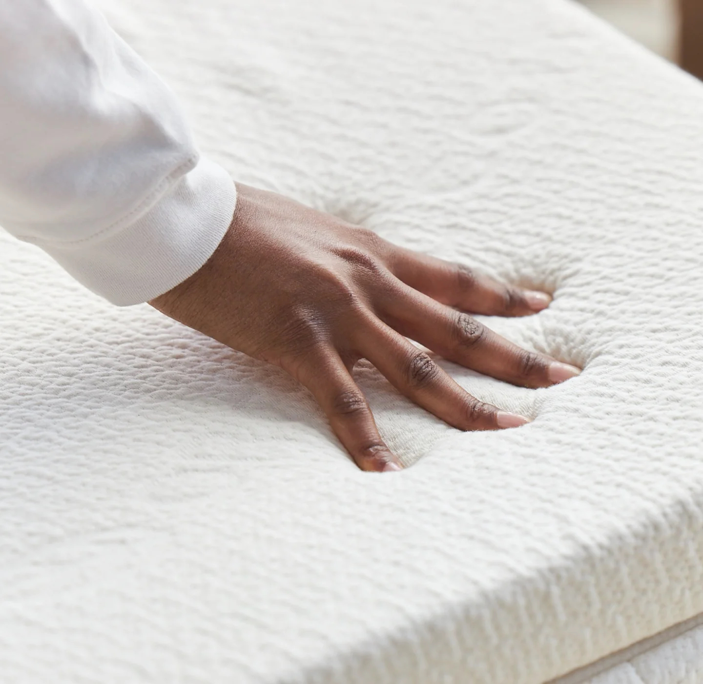 Hand pressing down on white mattress topper. 