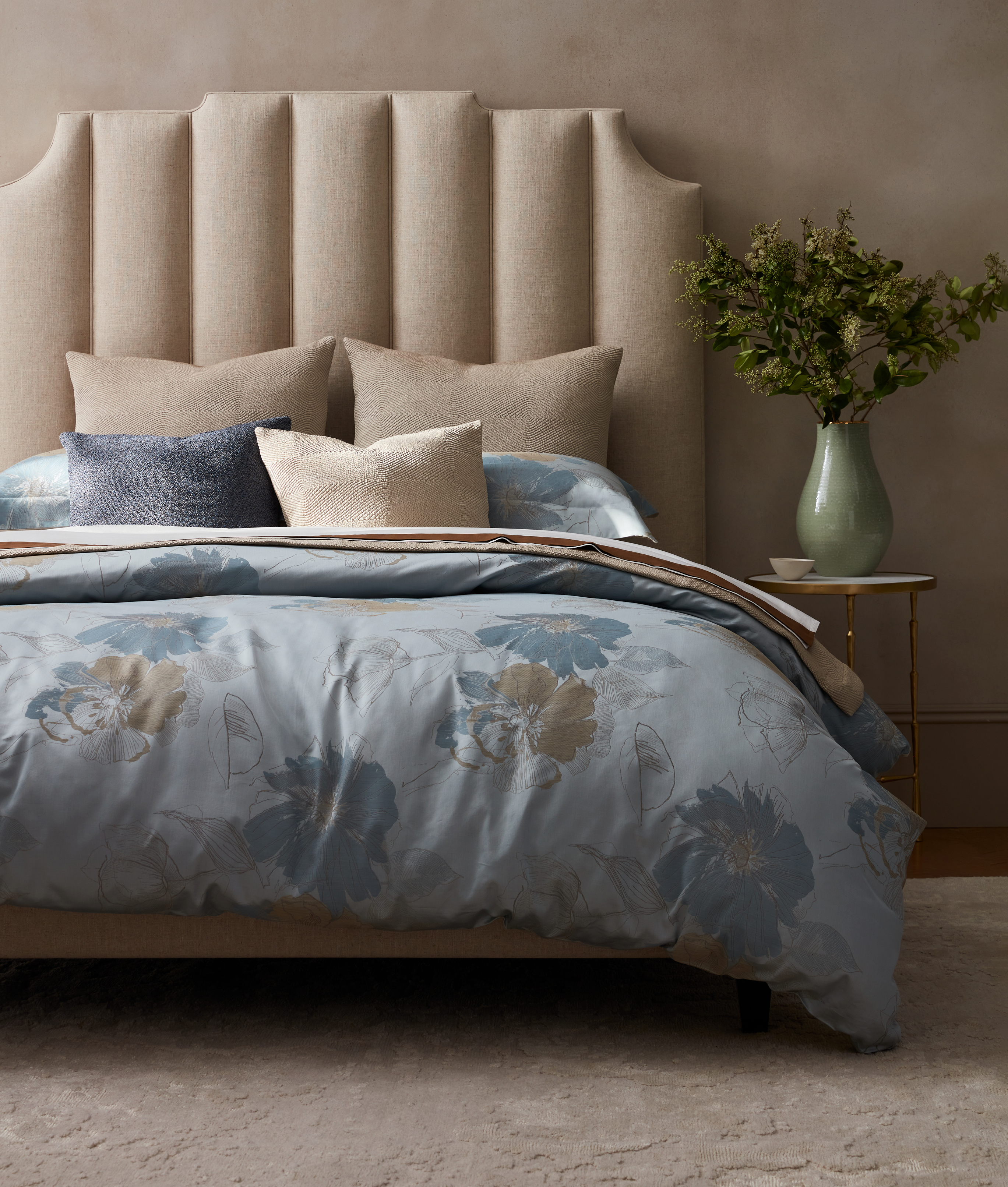 Bed with blue floral bedding and channeled beige headboard.